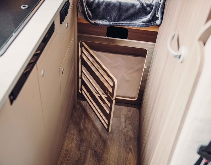 Carado motorhome interior with open storage hatch and laundry compartment next to the kitchenette