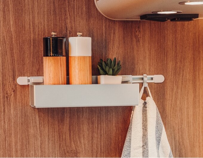 Wall shelf in the Carado motorhome with spice mills, a small plant and a hanging towel against a wood-effect décor