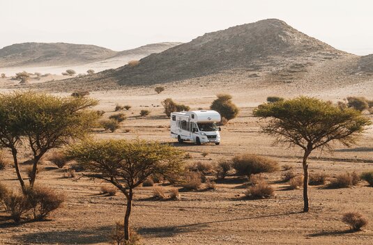 Carado motorhome in a sparse desert landscape with trees and rocky hills