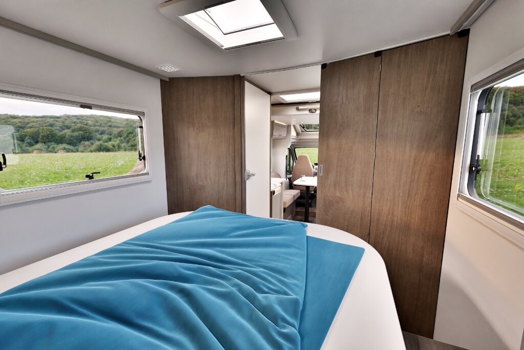 Sleeping area in the Carado motorhome with double bed, roof window and wood-finish cabinets