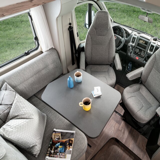 Seating group including driver's seats in the Exsis 580 with decorative cushions and magazine on the bench and dishes on the table