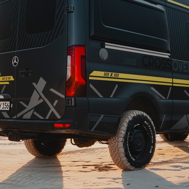 Side view of the rear axle of a camper van with black rims, all-terrain tires, 4x4 decal in neon green
