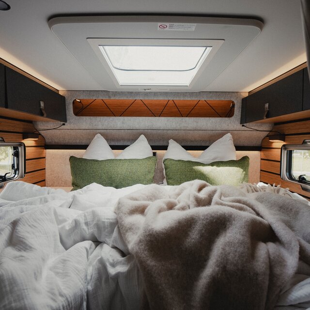 Sleeping area in a motorhome, made-up rear bed, two green decorative cushions and dark overhead cupboards