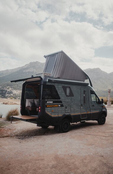 Vue de l'arrière du Venture S, avec le toit relevé et le Sunset Deck déployé, montagnes et eau en arrière-plan.