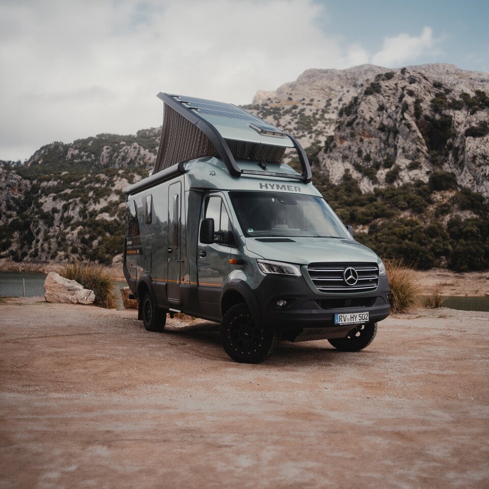 Vue de l'arrière du Venture S, avec le toit relevé et le Sunset Deck déployé, montagnes et eau en arrière-plan.