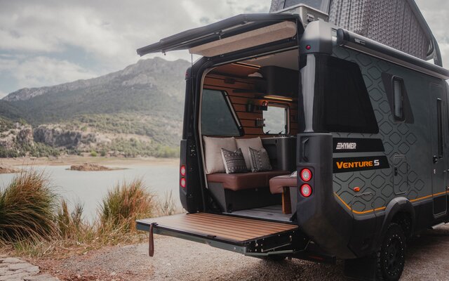Vue de l'arrière du Venture S, avec le toit relevé et le Sunset Deck déployé, montagnes et eau en arrière-plan.