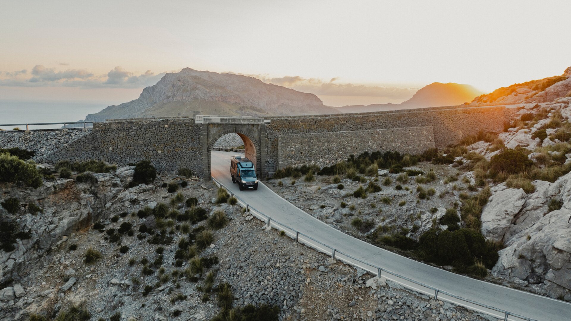 Vue d'en haut à l'avant du Venture S, le véhicule passe sous une arche, avec des montagnes et la mer en arrière-plan.