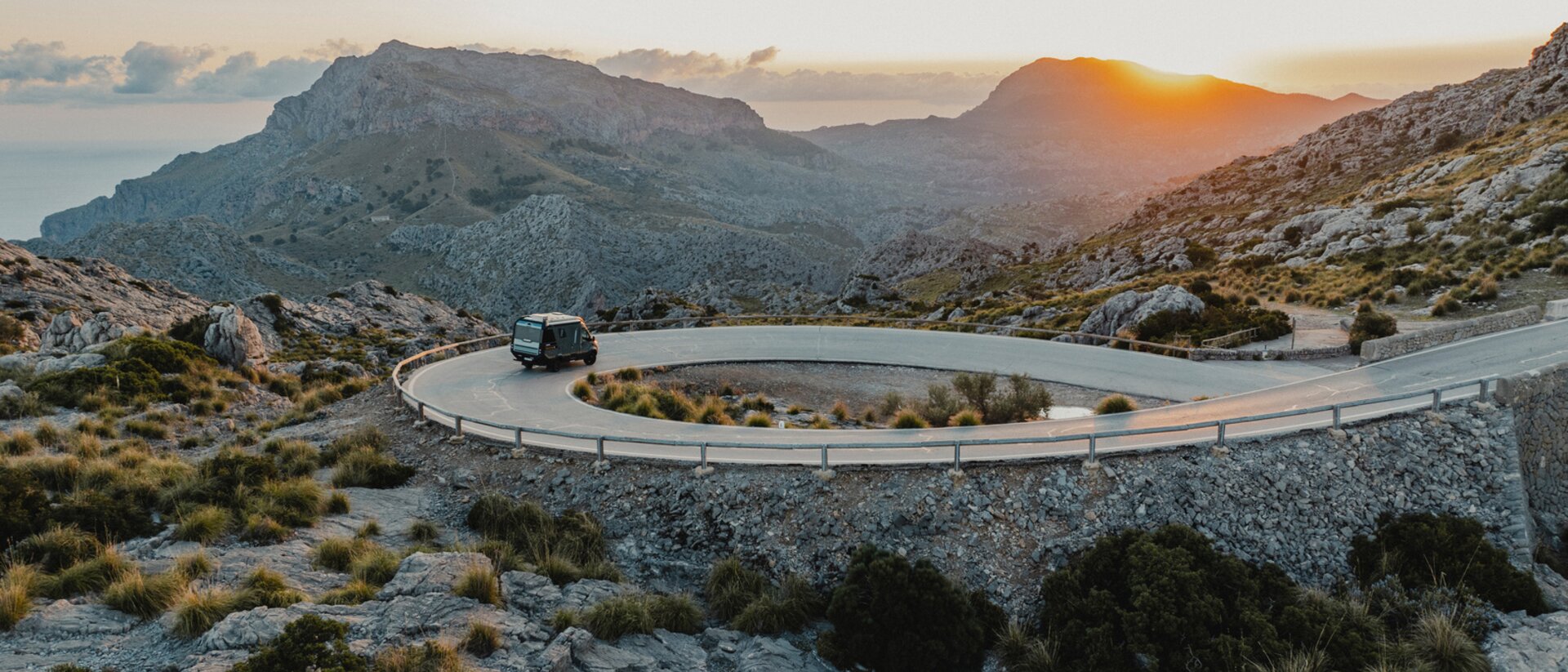 Vue de l'arrière du Venture S, le véhicule descend des routes sinueuses, avec des montagnes et la mer en arrière-plan.