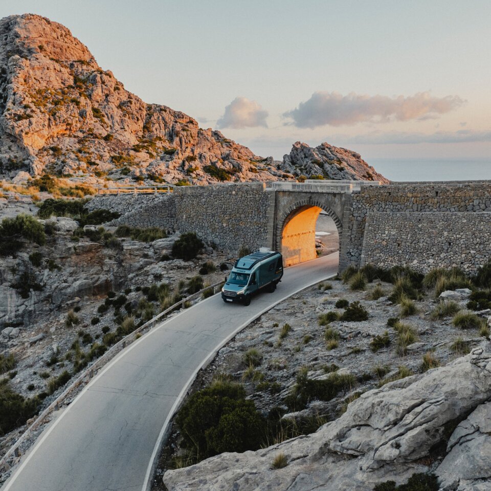 Vue d'en haut à l'avant du Venture S, le véhicule passe sous une arche, avec des montagnes et la mer en arrière-plan.