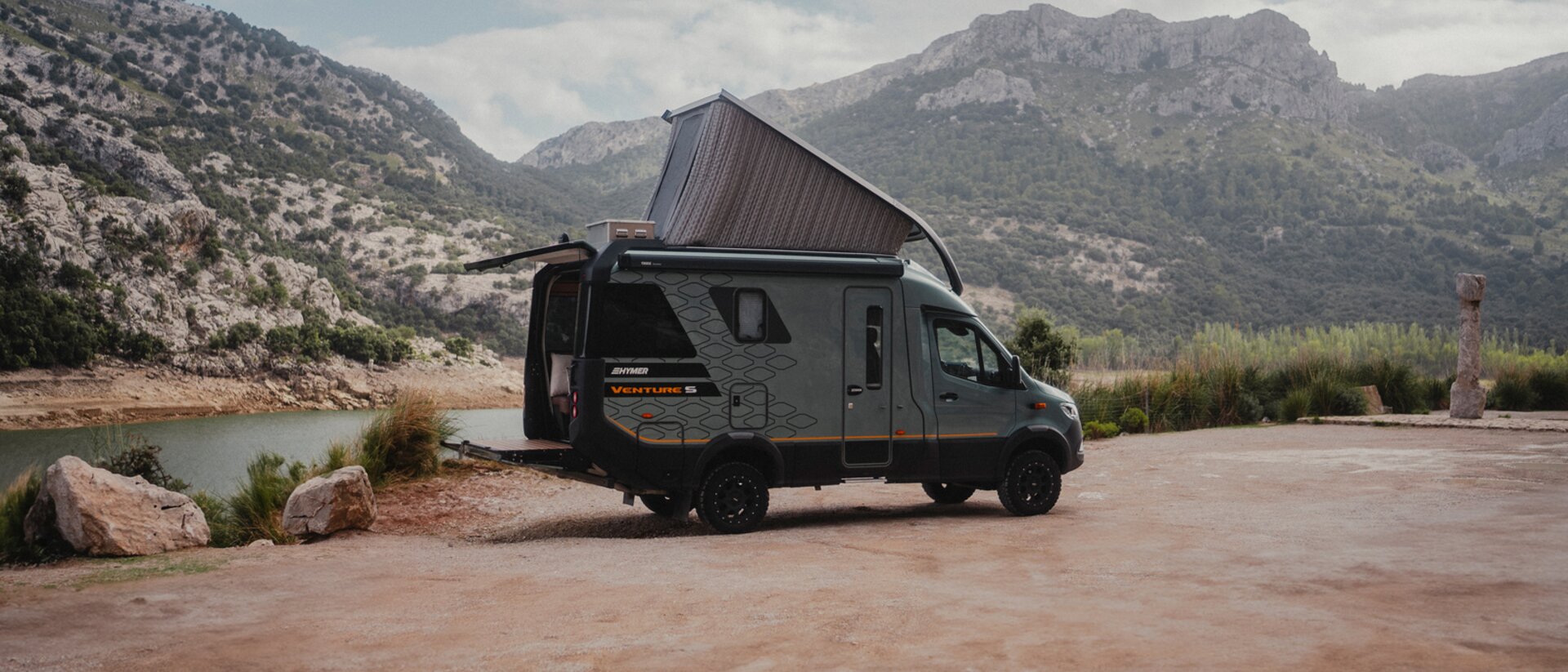 Vue latérale du côté passager du Venture S, avec le toit relevé et le Sunset Deck déployé, montagnes et eau en arrière-plan.