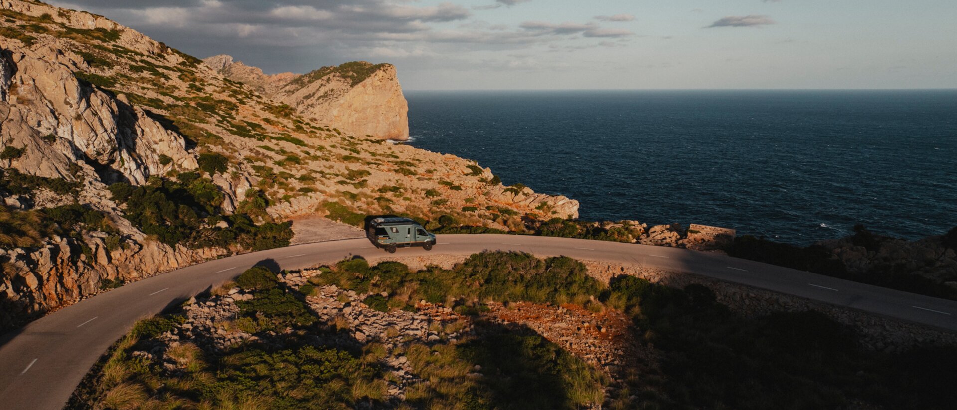 Vue aérienne du Venture S descendant des routes sinueuses, avec des montagnes et la mer en arrière-plan.