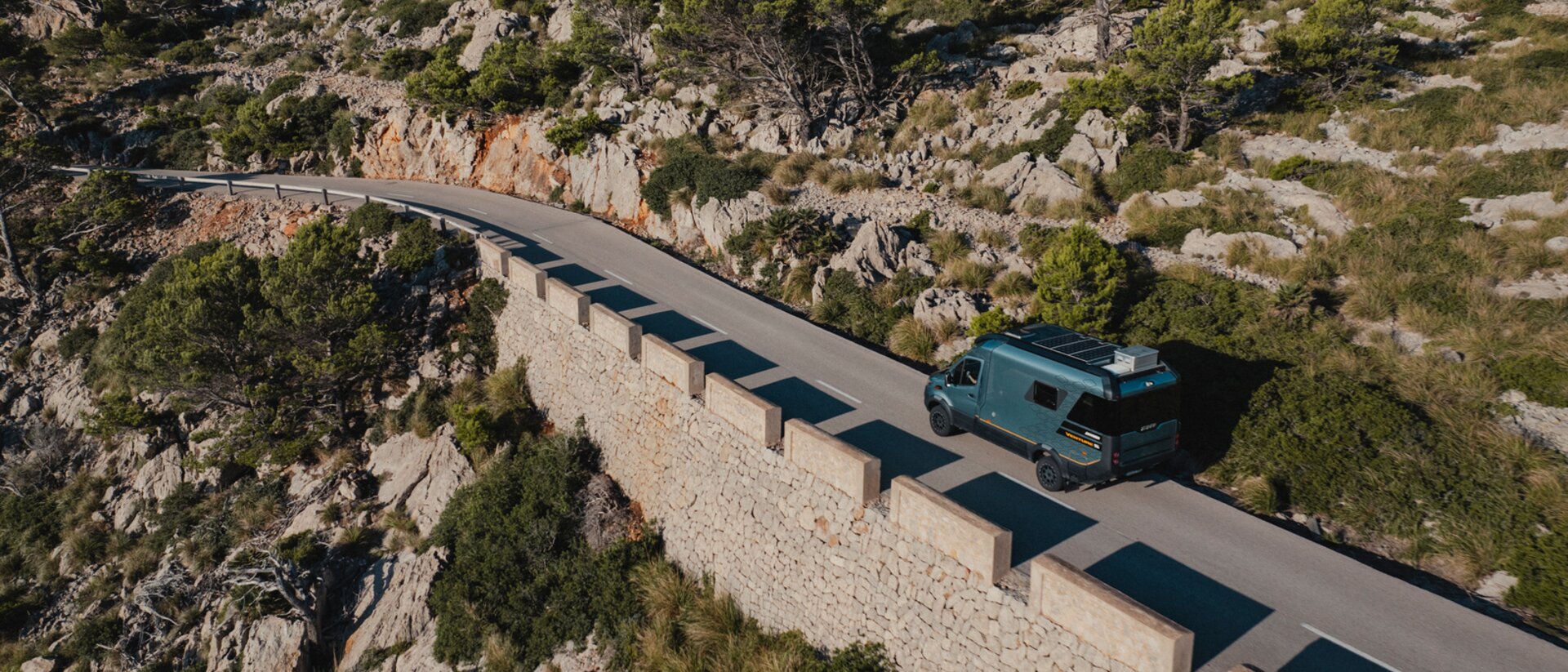 Vue aérienne du Venture S descendant des routes sinueuses, avec des rochers et des arbres en arrière-plan.