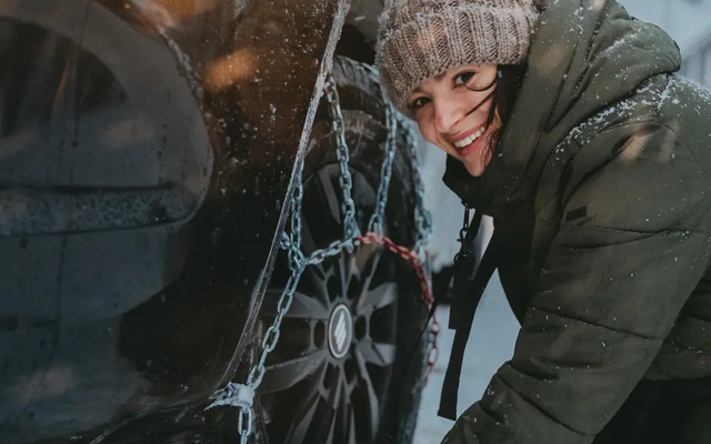 Uitzicht op een vrouw, ze legt sneeuwkettingen op een band