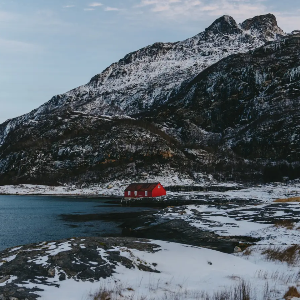 Solitair rood huis van een afstand op een rotsachtige zeekust