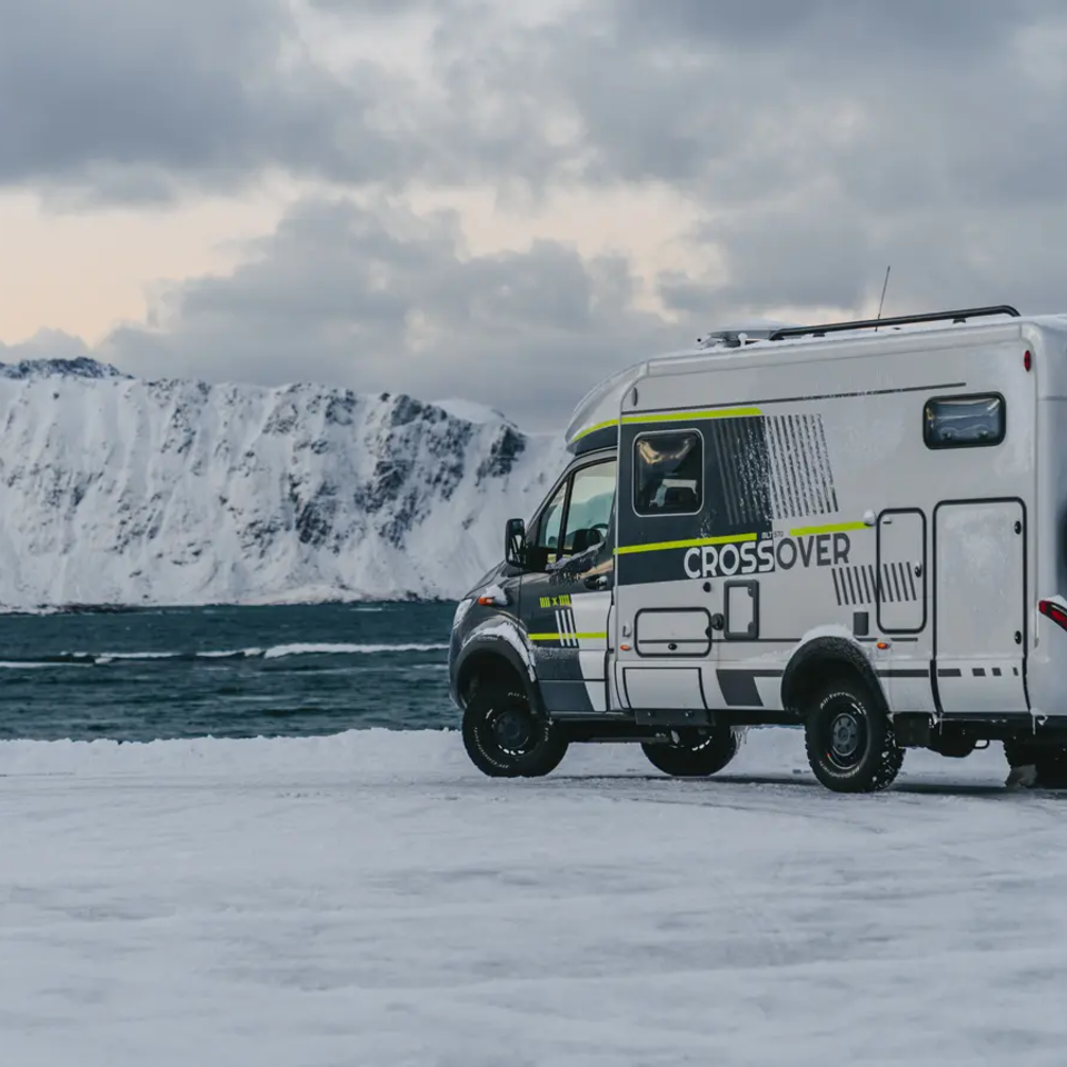 Zijaanzicht van de HYMER ML-T 570 CrossOver, hoge besneeuwde berg en de zee op de achtergrond