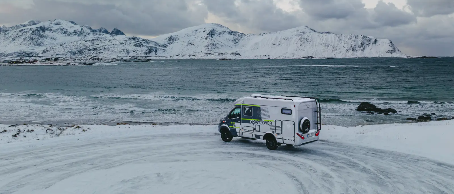 HYMER ML-T 570 CrossOver geparkeerd bij een uitkijkpunt, de zee en besneeuwde bergen op de achtergrond